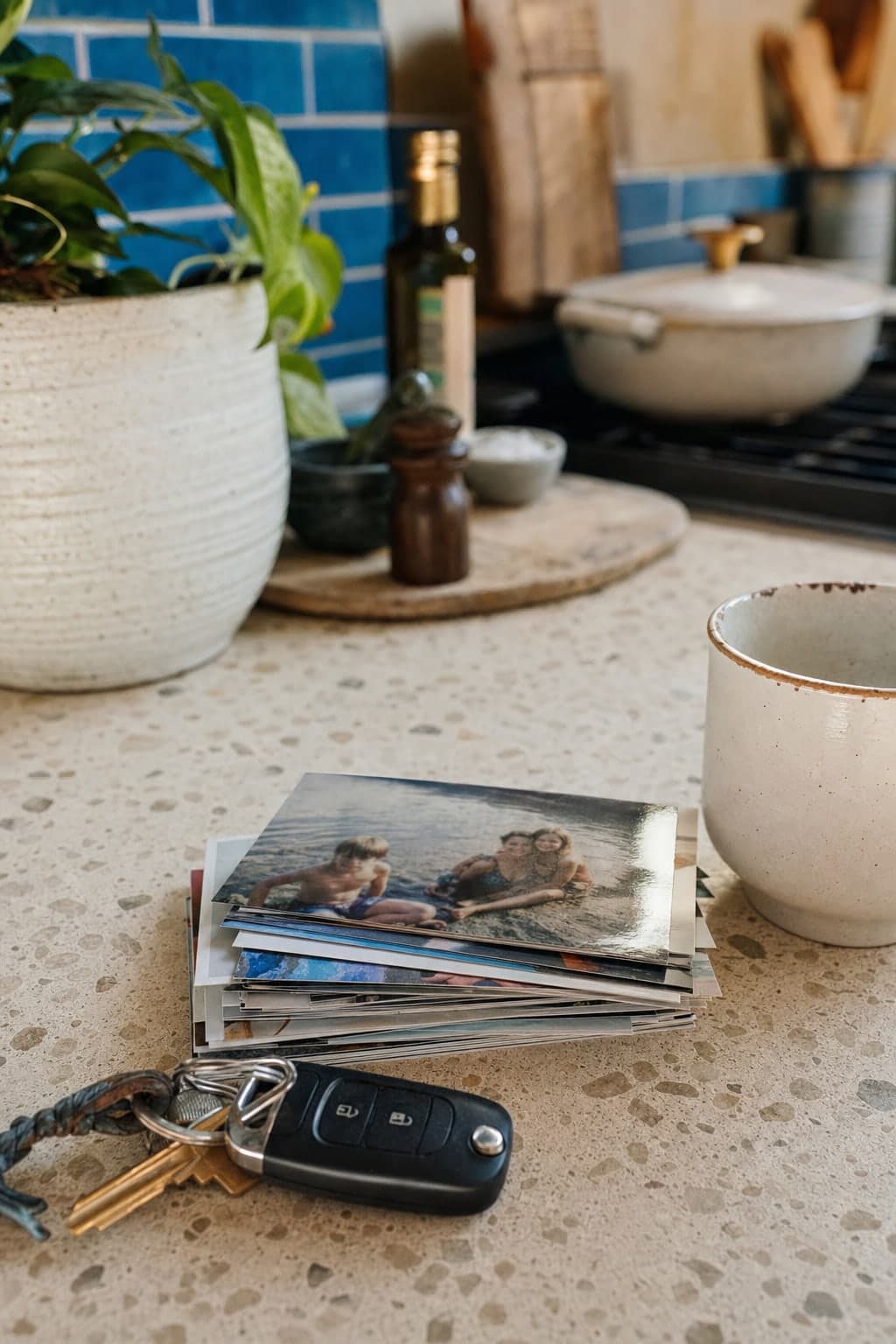 A stack of photo prints on a kitchen counter beside keys and a mug
